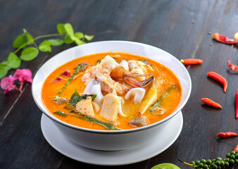 Tom Yam Kung or Tom Yum soup is Thai hot spicy soup shrimp or prawn with lemon grass, lemon, galangal, mushrooms, coconut milk and chili in bowl on wooden table top view, famous Thai food cuisine.