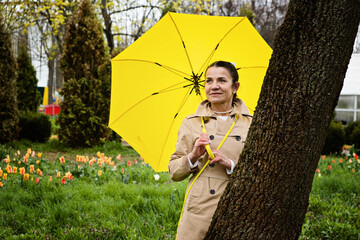 Stress resilience and mental health, concept. Managing stress and building resilience. Happy senior woman in yellow rain coat with yellow umbrella walking in park.