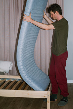 A man puts a mattress on a wooden bed 