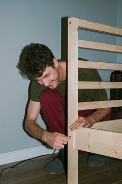A young man assembles a wooden bed 