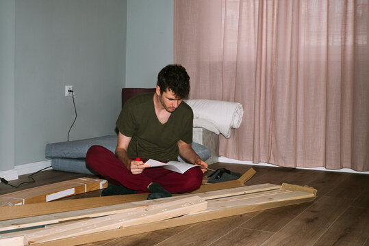 A curly-haired man studies the instructions for assembling a new bed