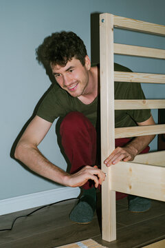 Smiling man assembles a wooden bed 