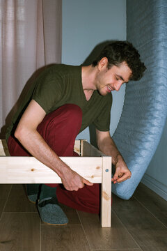 Smiling man assembles a wooden bed 