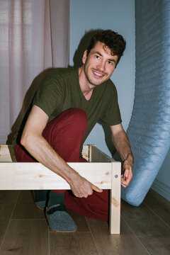 Smiling man assembles a wooden bed 