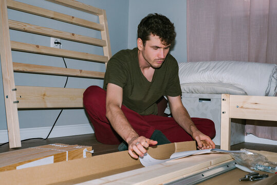 A curly-haired man studies the instructions for assembling a new bed