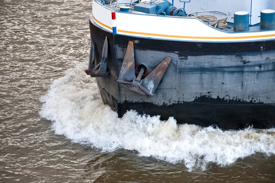 Detailansicht der Bugwelle und des Bugs mit gelichteten Ankern eines Binnenschiffs in voller Fahrt auf einem Fluss