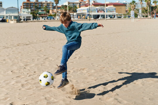 Boy kicking a soccer ball on a beach