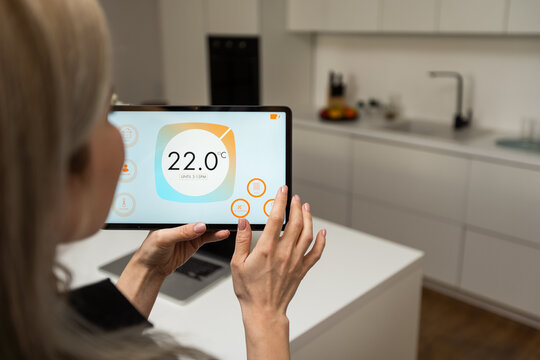 Woman pushing button on kitchen app of smart home on digital tablet at home. Concept of modern home control. Idea of domestic lifestyle. Cropped image of girl. Blurred man on background using laptop.