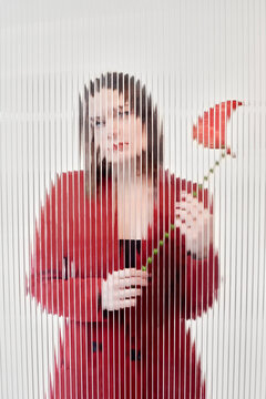 Woman standing behind the glass and holding red flower