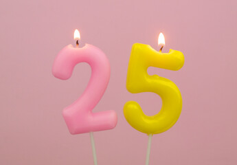 Burning birthday candles on pink background, number 25