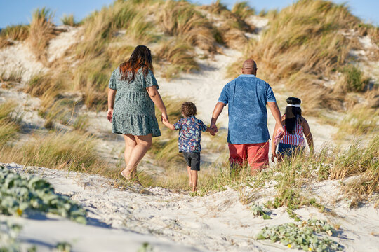 Family holding hands and walking on sandy beach path