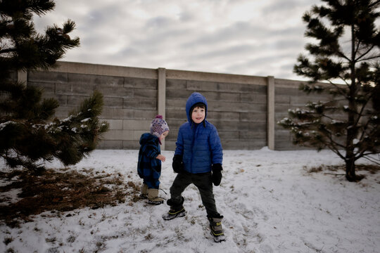 Two children playing in the snow in front of a wall