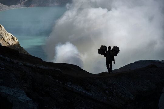 Silhouette of sulfur miner carrying heavy load of Sulphur at top of Kawah Ijen Volcano, Java, Indonesia