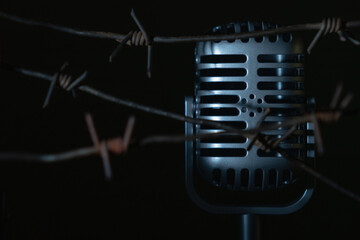 Close up microphone behind barbed wire as a symbol of discrimination, free speech crisis, political persecution and oppression. Copy space for text or design.