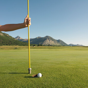 Detail of hand holding flag post at hole with golf ball