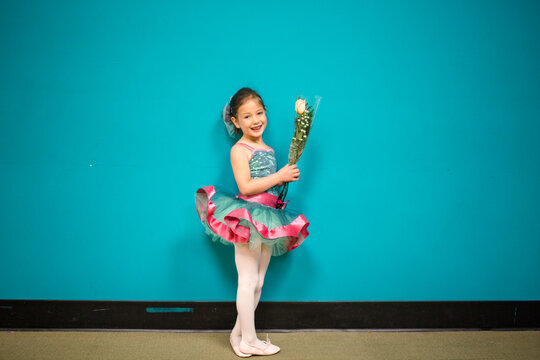A little girl stands in a dance costume holding a bunch of flowers