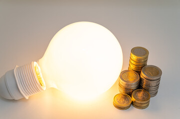 Light bulb turned off, with stacks of coins next to it. Rising electricity tariffs, energy...