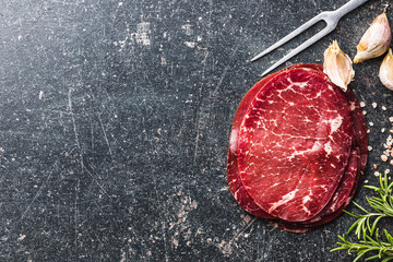 Smoked bresaola. Italian appetizer. Dried beef meat on black table. Top view.