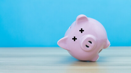 pink piggy bank flipped on its side indicating a financial crisis on a wooden floor.