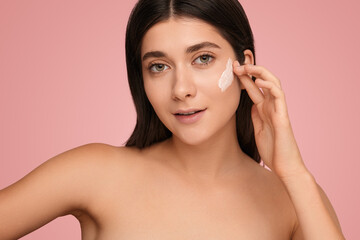 Young woman applying cream on face