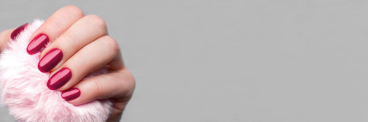 Female hand with pink fluffy ball with beautiful manicure - viva magenta, burgundy glittered nails banner with copy space. Wide panoramic header