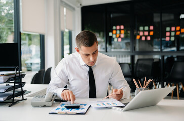 Young business man working at office with laptop, tablet and taking notes on the paper...