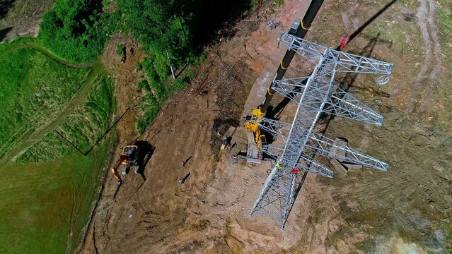 Crew of workmen working on a electrical transmission tower with a crane - aerial overlook