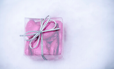 a small transparent box with heart-shaped chocolates inside, lying on the snow