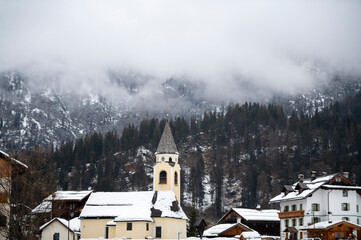 Heavy snow clouds hang over the snow-covered mountains and fir trees in the small mountain tourist...