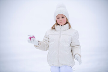 a little girl in winter white clothes in the snow holding a transparent box with candies in the shape of hearts