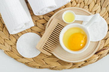 Small white bowl with raw egg and wooden hairbrush. Natural skin and hair care, homemade spa and beauty treatment recipe. Zero waste concept. Top view.