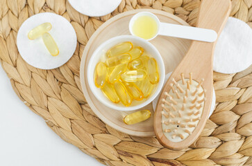 Small white bowl with cosmetic oil (face serum, fish oil) capsules and wooden hairbrush. Natural spa, skin and hair treatment recipe.