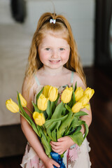 Happy little girl. Daughter congratulations and hold bouquet of yellow tulip flowers at home. Mother's, father day concept. Child girl smile. Greeting card for International Women's Day. Closeup.