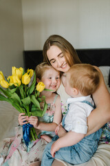 Obraz na płótnie Canvas Mother's day concept. Girl and boy congratulates mother and gives a bouquet of flowers tulips at home. Mom, son and daughter smiling and hugging. Holiday greeting card for International Women's Day.