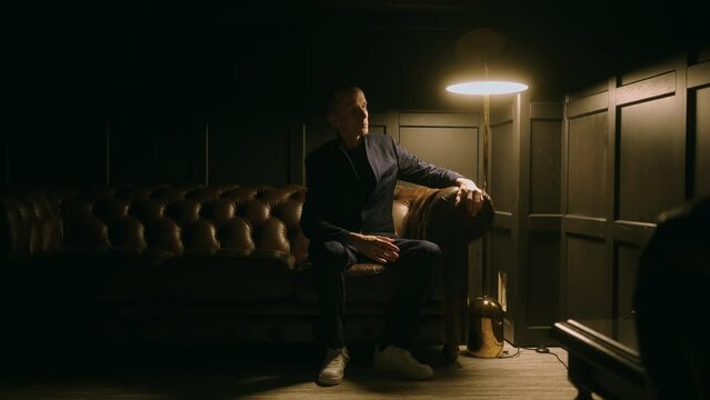 mad man moving like robot, sitting alone in dark room with table lamp, mysterious person