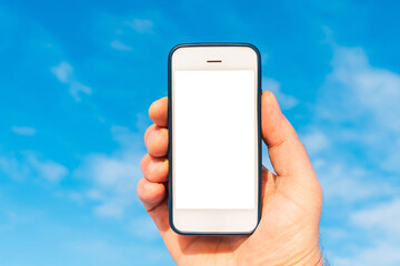 A Mans hand holding smartphone on blue sky nature background,sunny day. Mockup white screen smart phone.Copy space.