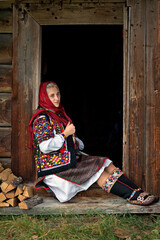Ukrainian girl in national Hutsul clothes sits on the threshold of an old wooden house