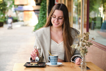 Young woman eating a cake and drinking coffee in a cafeteria.