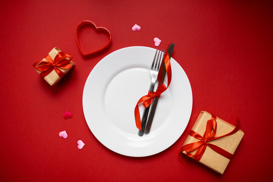 classic festive table setting in valentine's day style with gifts and hearts on a red background. copy space. top view. 14 february concept