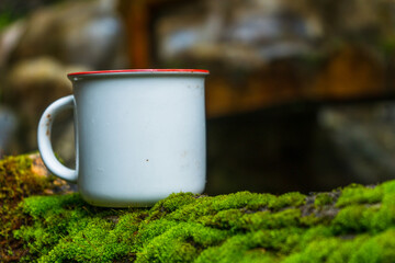 An enamel mug standing out on the top of green moss with out of focus rock background