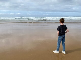 child standing on the beach watching the sea