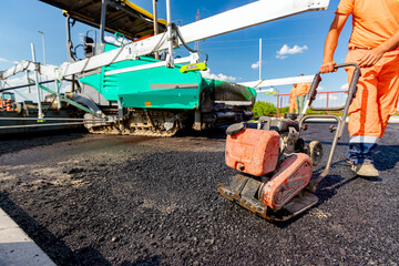 Worker compacts tarmac using vibration plate compactor