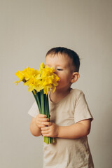 a child sniffs a bouquet of yellow daffodils