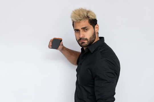 Serious businessman holding smartphone. Male Caucasian model with brown eyes, ombre painted hair and beard in black shirt holding his smartphone screen down. Modern technology concept