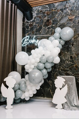 Birthday decorations - arch, balloons, and decor for little baby party on a wall background. Celebration baptism concept. Baby text. Photo zone with angel for babe shower. Photo area in silver style.