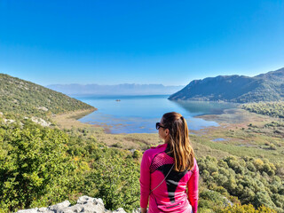 Naklejka premium Rear view of woman with panoramic view of Lake Skadar National Park in autumn seen from Virpazar, Bar, Montenegro, Balkans, Europe. Stunning travel destination in Dinaric Alps near Albanian border