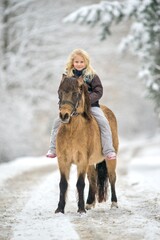 A young girl is riding a horse in winter