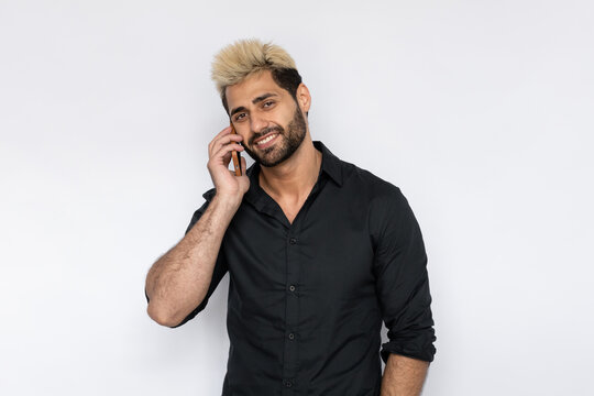 Winsome young man talking on mobile phone. Male Caucasian model with brown eyes, ombre painted hair and beard in black shirt speaking on phone. Communication, modern technology concept