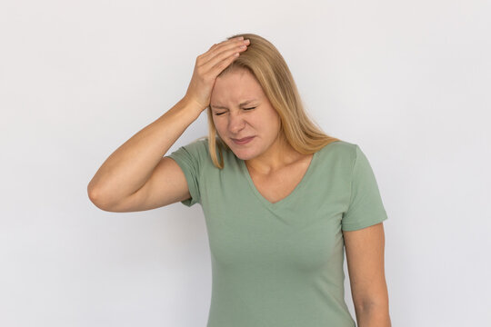 Stressed young woman with hand on forehead. Portrait of frustrated Caucasian female model with fair hair in green T-shirt with closed eyes realizing mistake. Regret, stress, headache concept