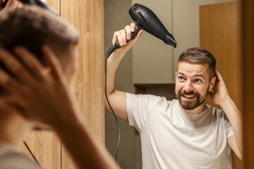 Reflection of a happy man drying his hair with hairdryer in bathroom.